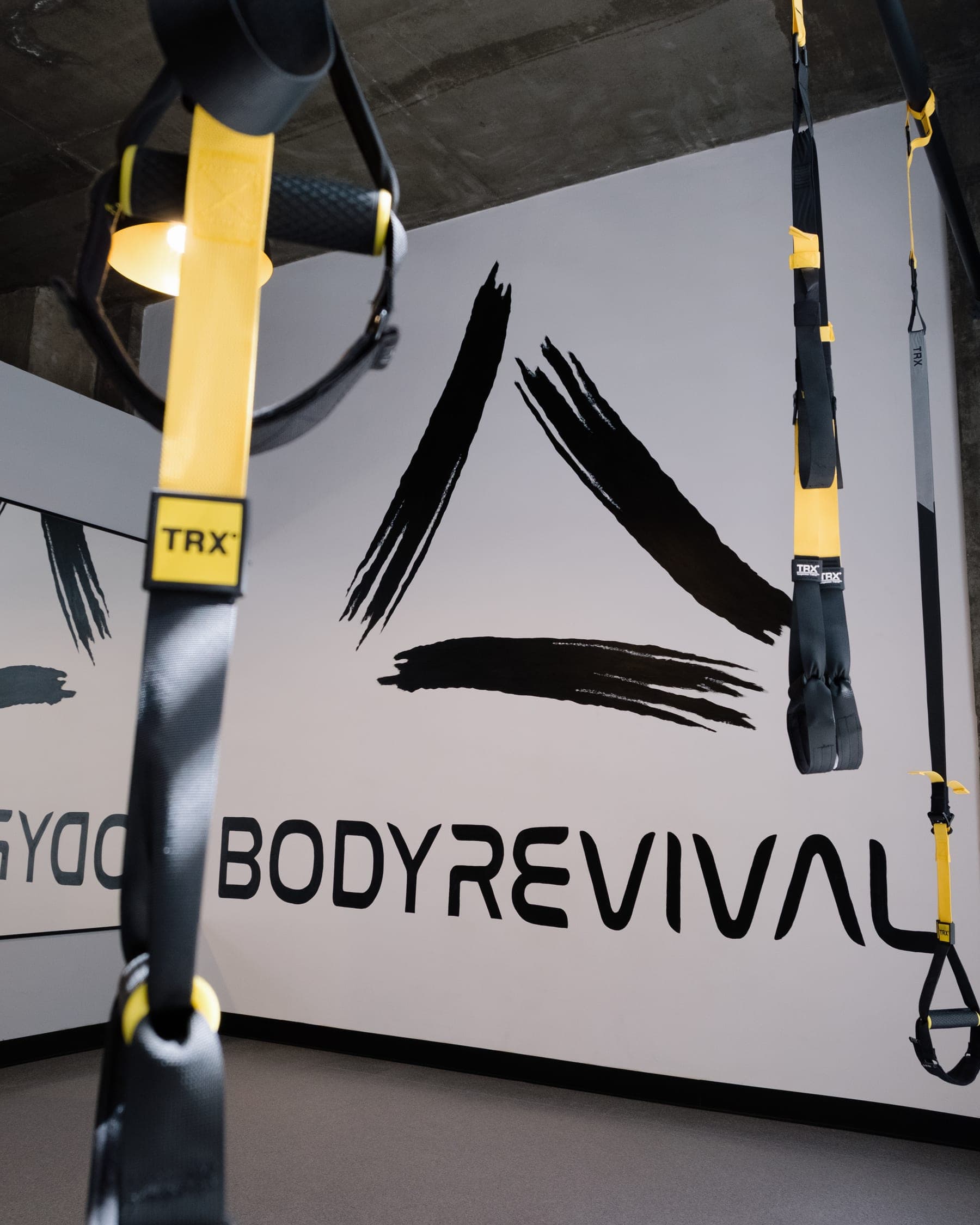 Body Revival divarının qarşısında asılı TRX lentləri